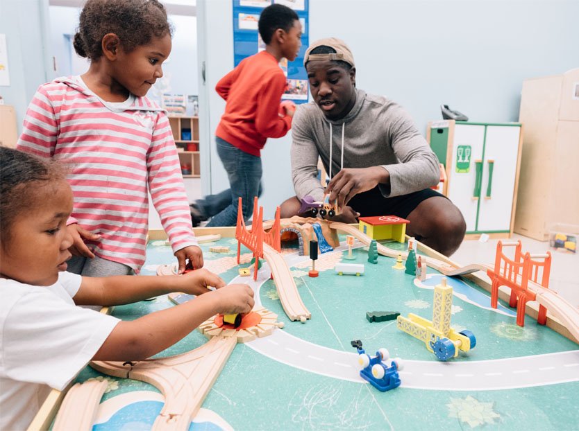 Man playing with toy trains with children