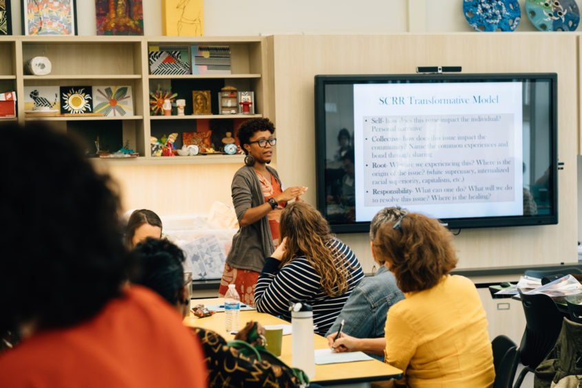 An African American woman stands in front of a crowd, presenting information on personal development.