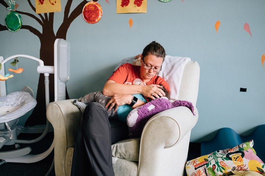 Image: An early learning professional holds a baby in her arms, with one hand gently caressing the child's head.