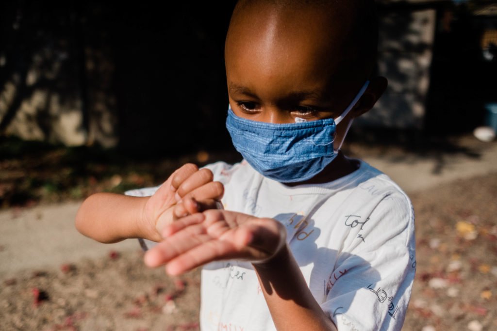 child wearing a mask holds out their hand