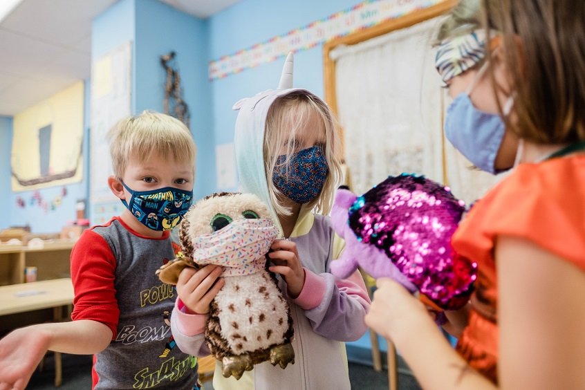 Image: Two young children show their early learning teacher a stuffed animal. The teacher responds by showing them her stuffed animal.