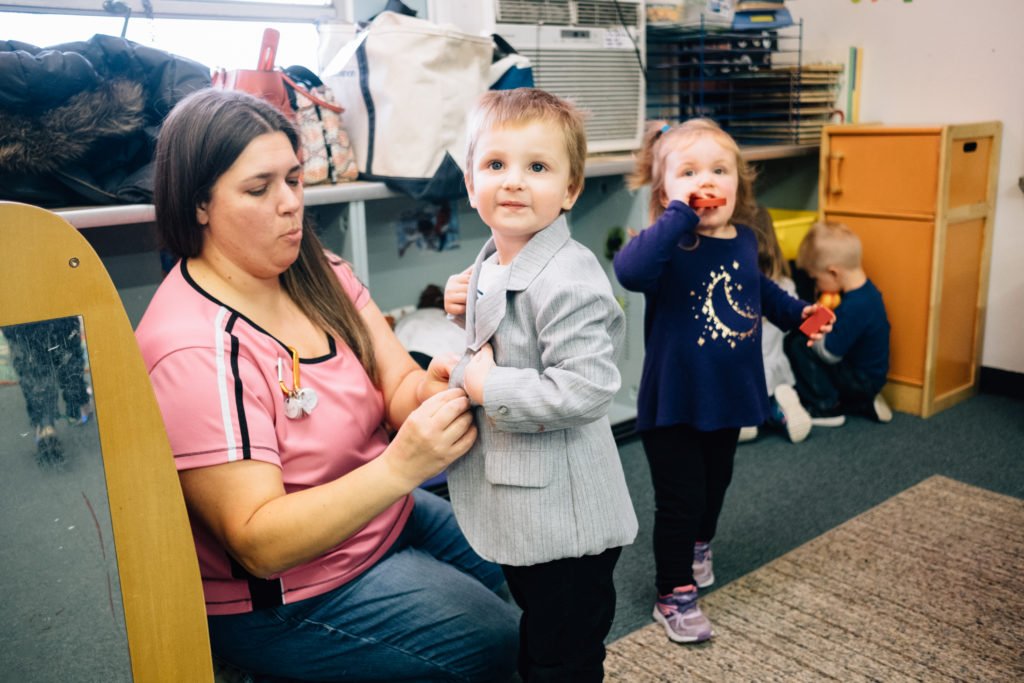 Caregiver helping a child put on a coat | identity development