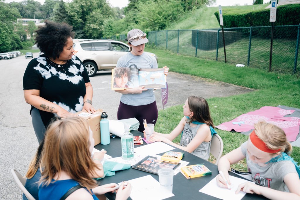 Two instructors standing at a table in front of children explaining a drawing | Pittsburgh LGBTQ+ organizations