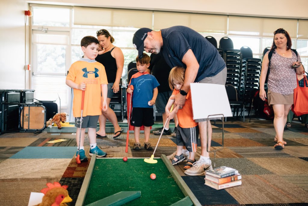 Father figure plays mini golf with two young boys | blended families
