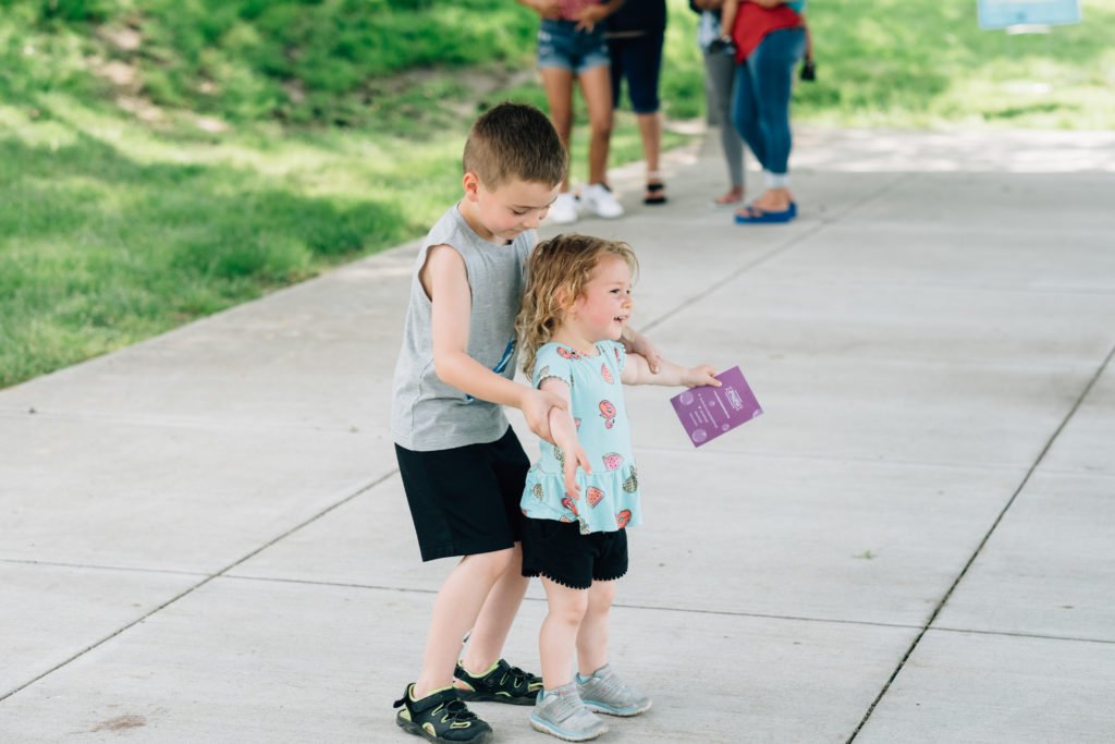 Two children playing, one older boy stands behind younger girl and dances | sibling relationships
