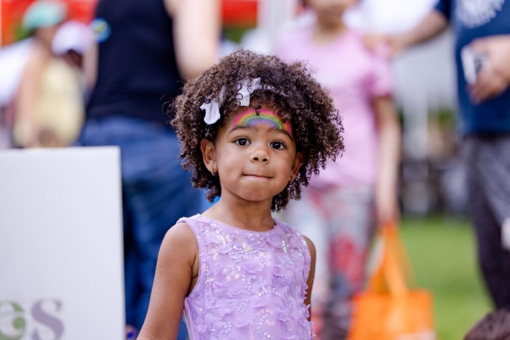 A little girl with curly and a rainbow painted on her face looks at the camera | How Culturally Rich Dramatic Play Supports Language Development