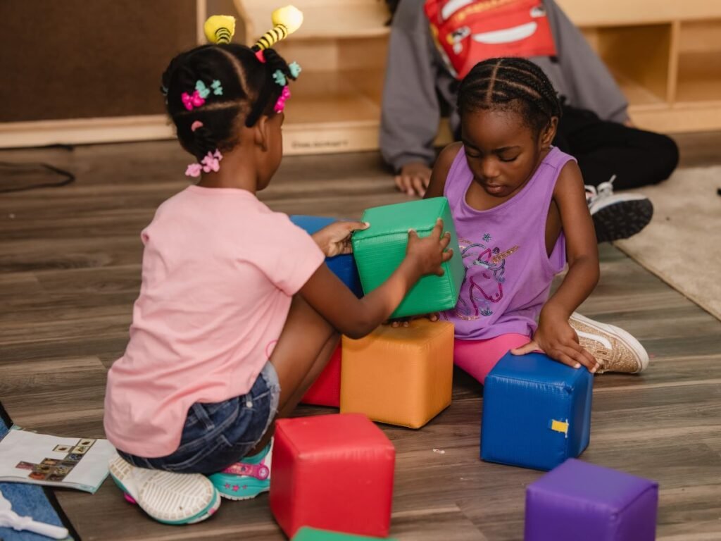Two young girls sitting on the floor playing with large blocks | How Play Fosters Social and Cognitive Development in Children