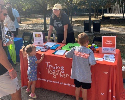 An adult stands behind a table talking to two children